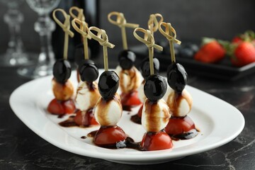 Tasty canapes with black olives, mozzarella and cherry tomatoes on dark textured table, closeup