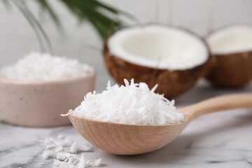 Coconut flakes in wooden spoon on white marble table, closeup