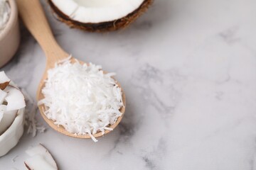 Coconut flakes in wooden spoon on white marble table, closeup. Space for text