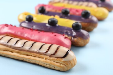Delicious eclairs covered with glaze on light blue background, closeup
