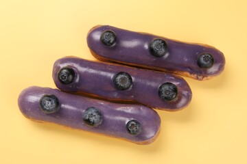 Delicious purple eclairs decorated with blueberries on yellow background, top view
