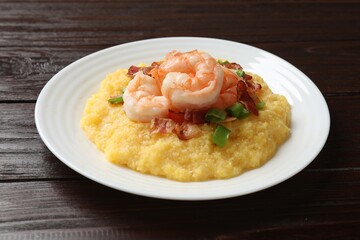 Plate with fresh tasty shrimps, bacon, grits and green onion on dark wooden table