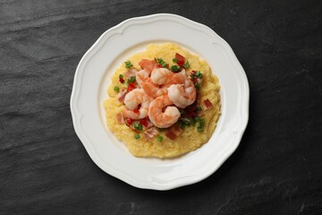 Plate with fresh tasty shrimps, bacon, grits, green onion and pepper on black textured table, top view