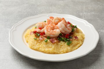 Plate with fresh tasty shrimps, bacon, grits, green onion and pepper on gray textured table, closeup