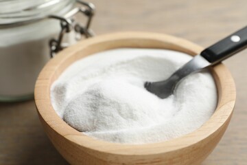 Baking soda in bowl on wooden table, closeup