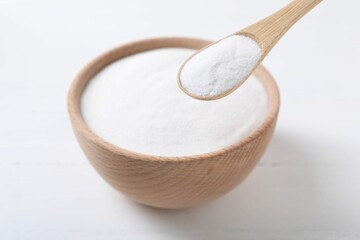 Taking baking soda from bowl at white wooden table, closeup
