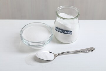 Baking soda in bowl, glass jar and spoon on white wooden table
