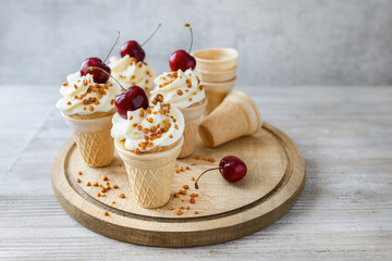 Cherry cone cakes with cream cheese frosting and nuts, kids summer party food on wooden board front view