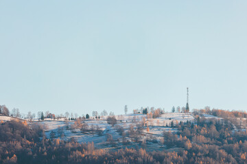A majestic snow-covered hill rises with grace, its peak adorned by a towering radio tower under the wintry sky
