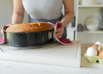 Woman serving a fresh and hot bundt cake in a baking pan on kitchen counter