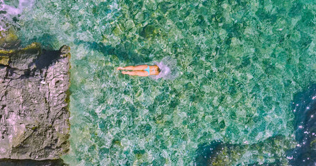 AERIAL: A slow motion shot of a young woman head diving into the turquoise water