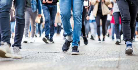 A crowd of people walking on the sidewalk, some holding phones and looking at their screens. A high resolution photo with focus on one person in motion