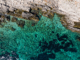 TOP DOWN: Flying directly above the rocky ledges meeting the turquoise sea.