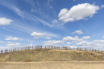 Rural scene of a broken weathered old wooden fence curving with the hilltop under a blue sky with...