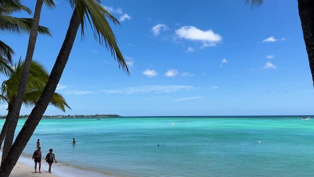 Magnificent turquoise sea through palm trees on Trou aux biches beach on the tropical island of Mauritius. A couple walking on the white sand beach