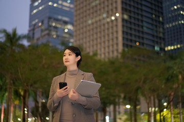 Confident Businesswoman in City at Dusk with Technology