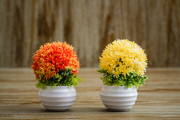 Vibrant, artificial orange,yellow flower arrangements placed on a rustic wooden surface, potted in...