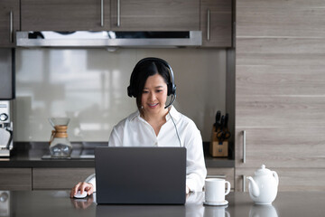 Young Asian professional woman working from home on her laptop while sipping a hot drink.