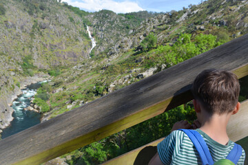 A boy on a sunny day looks at the Douro river valley, Portugal, rocky mountain and waterfall