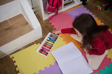 View from above of a little child girl taking out colorful pencils from a box, drawing picture at...