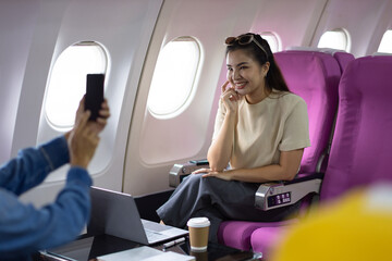 Young Asian woman and friends sitting talking and taking travel photos while in flight. Young female tourists and friends enjoying an amazing trip in Asia use their mobile phone to take a photo.