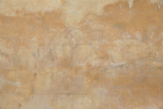 Old rough yellow ochre colored cracked painted plaster wall texture. Shabby earth coloured grunge texture, building facade. Closeup of historical house detail. Faded stained beige backdrop.