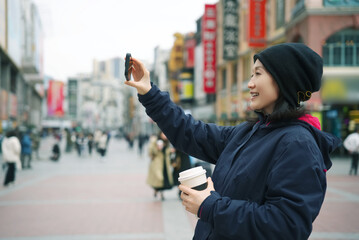 Young Woman Enjoying Coffee and Taking Selfie on City Street