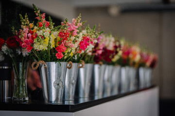 Dobele, Latvia - August 18, 2023 - A row of colorful flowers in metal buckets on a black countertop...