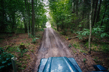 Dobele, Latvia - August 18, 2023 - Driver's perspective on a forest road from inside an off-road vehicle, surrounded by dense trees.