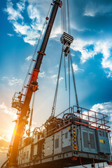 Fototapeta premium Industrial Crane operating and lifting an electric generator against sunlight and blue sky 