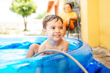 Happy child playing in inflatable home pool in summer. Active outdoor recreation.
