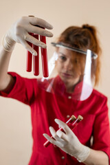 Caucasian woman doctor wear red uniform in medical mask, gloves  holding test tube with red liquid