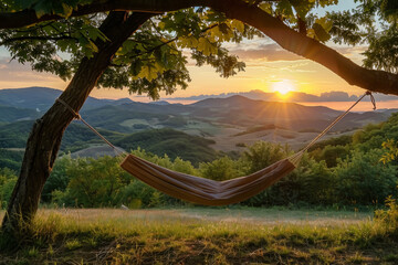 Fototapeta premium Hammock suspended between trees with a view of rolling hills and sunset in tranquil countryside setting.