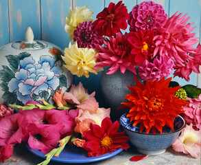 still life of dahlias and gladioli in a vase on a marble table with blue painted background. © Erika