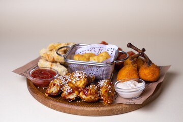 Crispy chicken wings, potato balls, cheese sticks with sauces on wooden platter