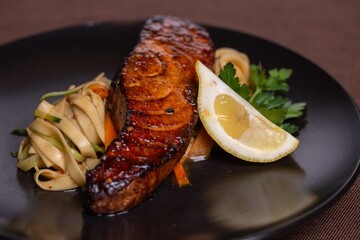 Grilled salmon with lemon and vegetables on a black plate