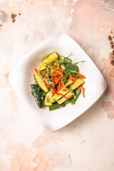 Fresh cucumbers, bell peppers, and herbs on white plate, pink background