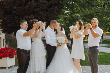 A group of people are posing for a picture, with a bride and groom in the center. The bride is...