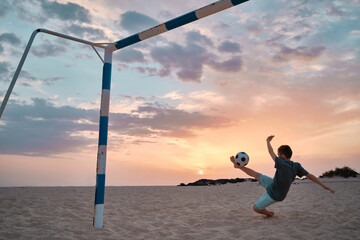 Boy playing football on the sand on beach outdoors, players in soccer in dynamic action have fun...