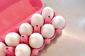 White chicken eggs in a pink egg tray. Fresh organic chicken eggs in an open carton or egg container, set 10 of 12, stock photo in the kitchen.