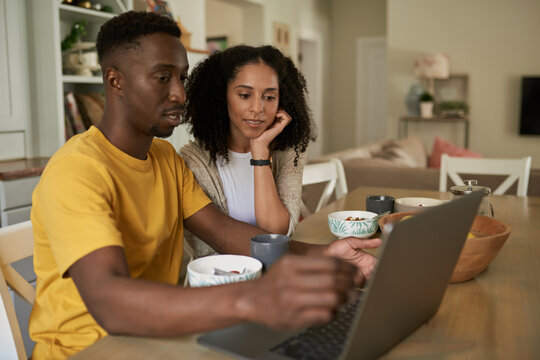 Young multiethnic couple using a laptop during breakfast in the morning - Powered by Adobe