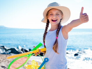Child in hat on beach shows thumb up - 800248375