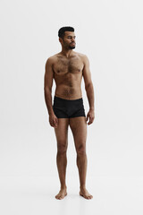 Fototapeta premium Full-length image of handsome African-American man standing shirtless in black boxes isolated on white background. Masculinity. Concept of male beauty, sport, body care, health, fitness
