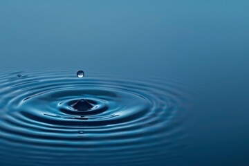 Water droplet with water ripples below the surface of blue water, small circular shape floating above it