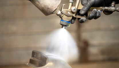 Close-up image of a skilled worker's gloved hands using a professional spray gun to paint a car...