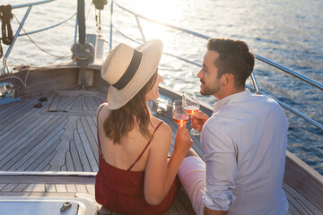 Couple in love drinking wine on yacht by sea. Travel on sailboat at sunset. Happy travelers...