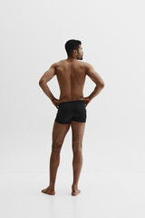 Fototapeta premium Back view. Young African-American man with relief strong back, muscular body standing in black boxers isolated on white background. Concept of male beauty, sport, body care, health, fitness