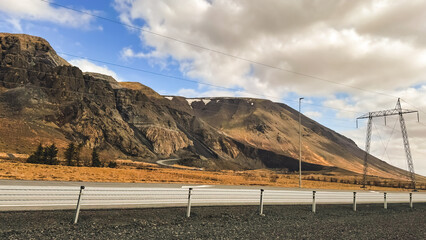 Photo of Icelandic landscapes, a high mountain along a route with power transmission. Volcanic mountains, against the backdrop of a beautiful sky with clouds.