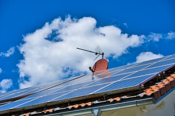 roof of house with photovoltaic system and satellite dish in the background blue sky and clouds