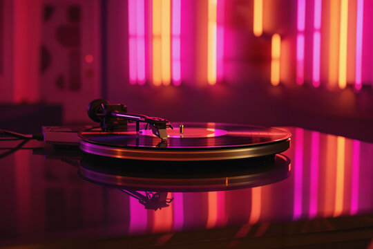 Old fashioned turntable with record. Vintage turntable, vinyl record player in neon lights. Reflecting light in a nightclub.